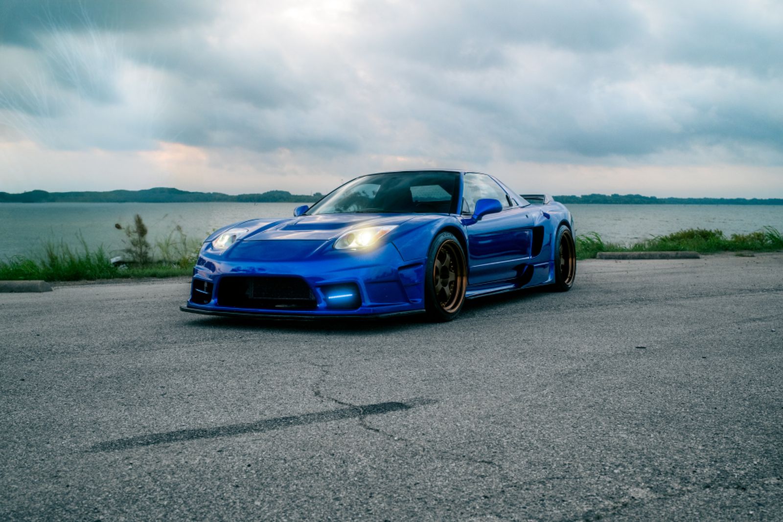 Blue widebody 1992 Acura NSX parked by a lake under a cloudy sky